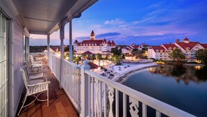 A balcony with white chairs, a view of a large building with multiple red roofs, and a calm body of water. - The Villas At Disney's Grand Floridian Resort & Spa (Lake Buena Vista)