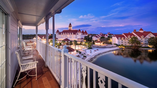 A balcony with white chairs, a view of a large building with multiple red roofs, and a calm body of water. - The Villas At Disney's Grand Floridian Resort & Spa (Lake Buena Vista)