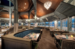En rummelig restaurant med højt til loftet, træbjælker og store vinduer der giver udsigt over bybilledet.