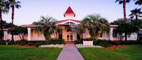 A building with a red roof, a central entrance, and palm trees.