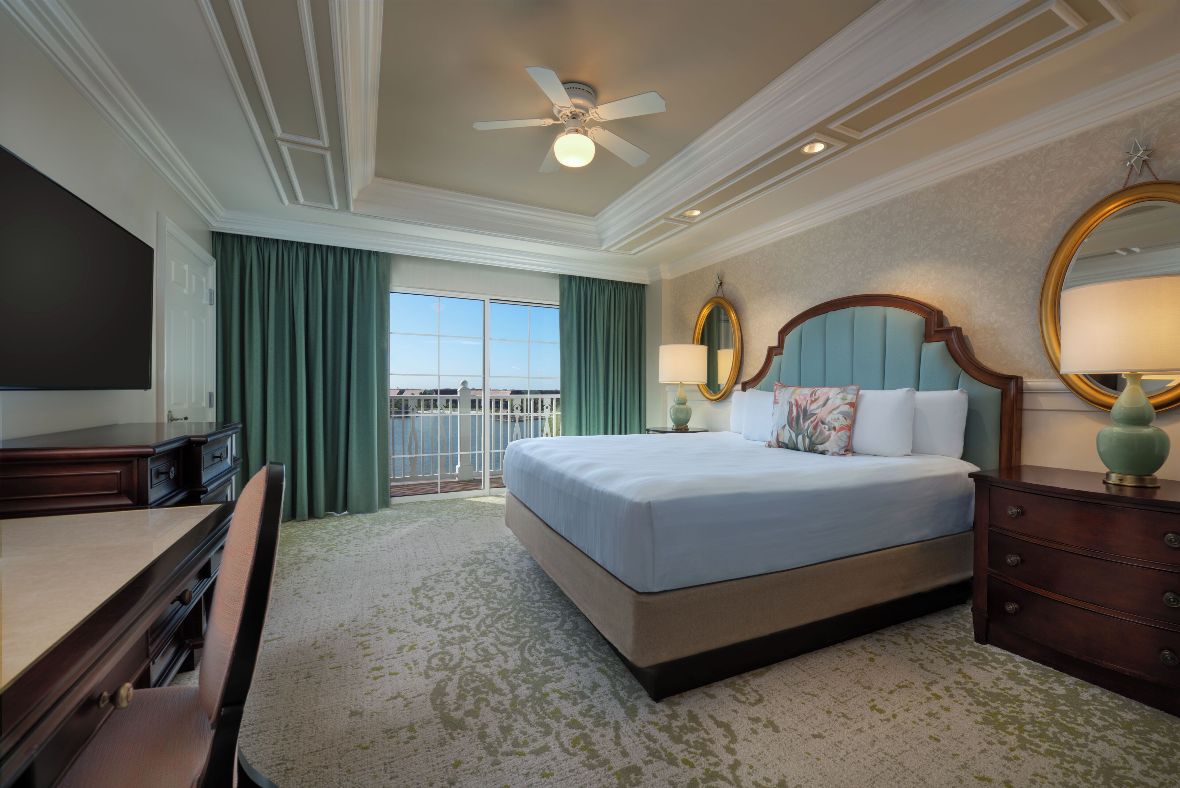 Une chambre d’hôtel avec un grand lit, un bureau, une chaise, une télévision, un ventilateur de plafond et une vue sur l’extérieur.