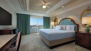 Une chambre d’hôtel avec un grand lit, un bureau, une chaise, une télévision, un ventilateur de plafond et une vue sur l’extérieur.