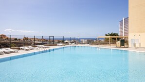 Una gran piscina al aire libre con sillones de descanso y vistas al océano y edificios.
