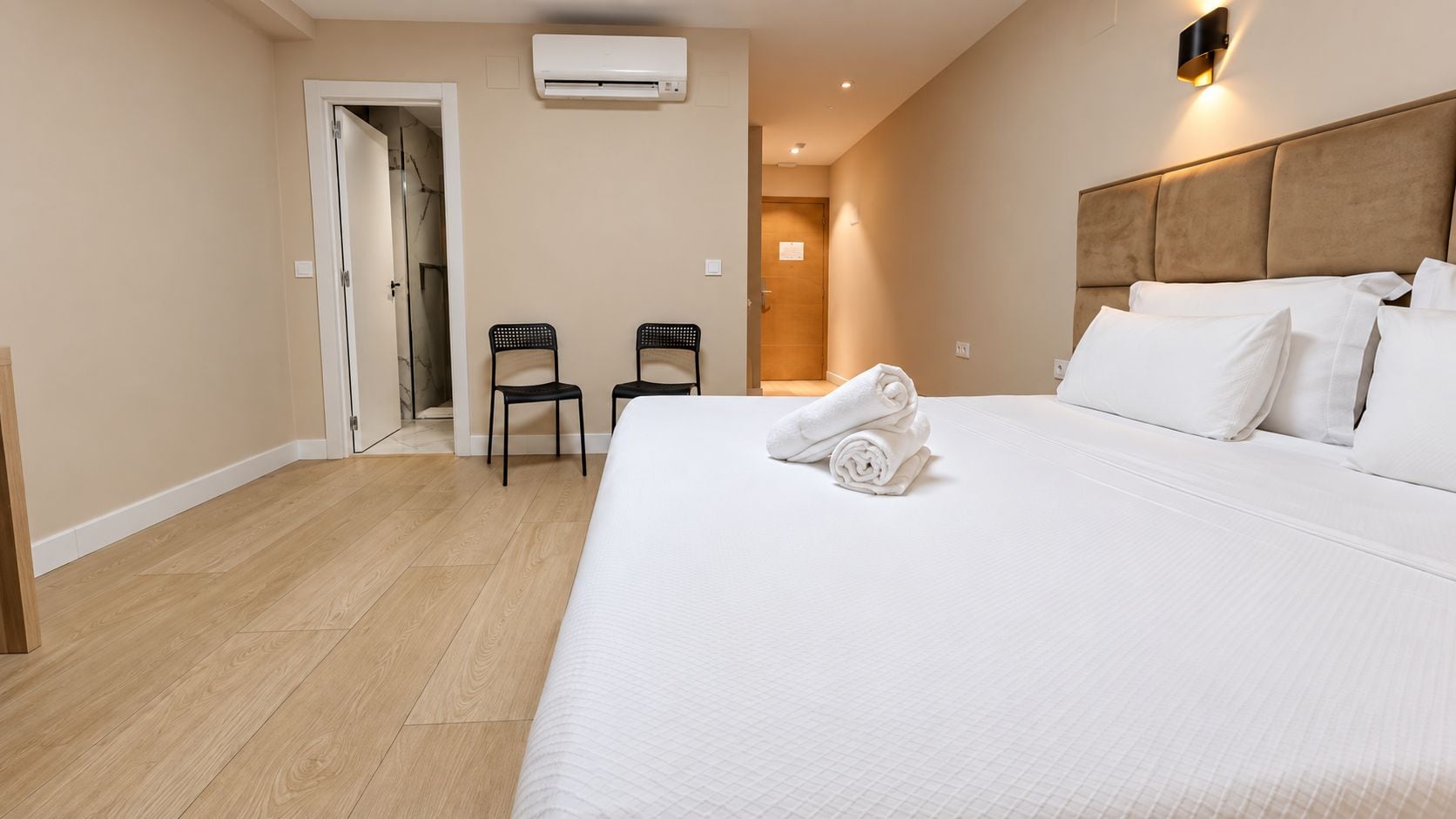 Una habitación de hotel con una cama grande, dos sillas, una puerta y un equipo de aire acondicionado.