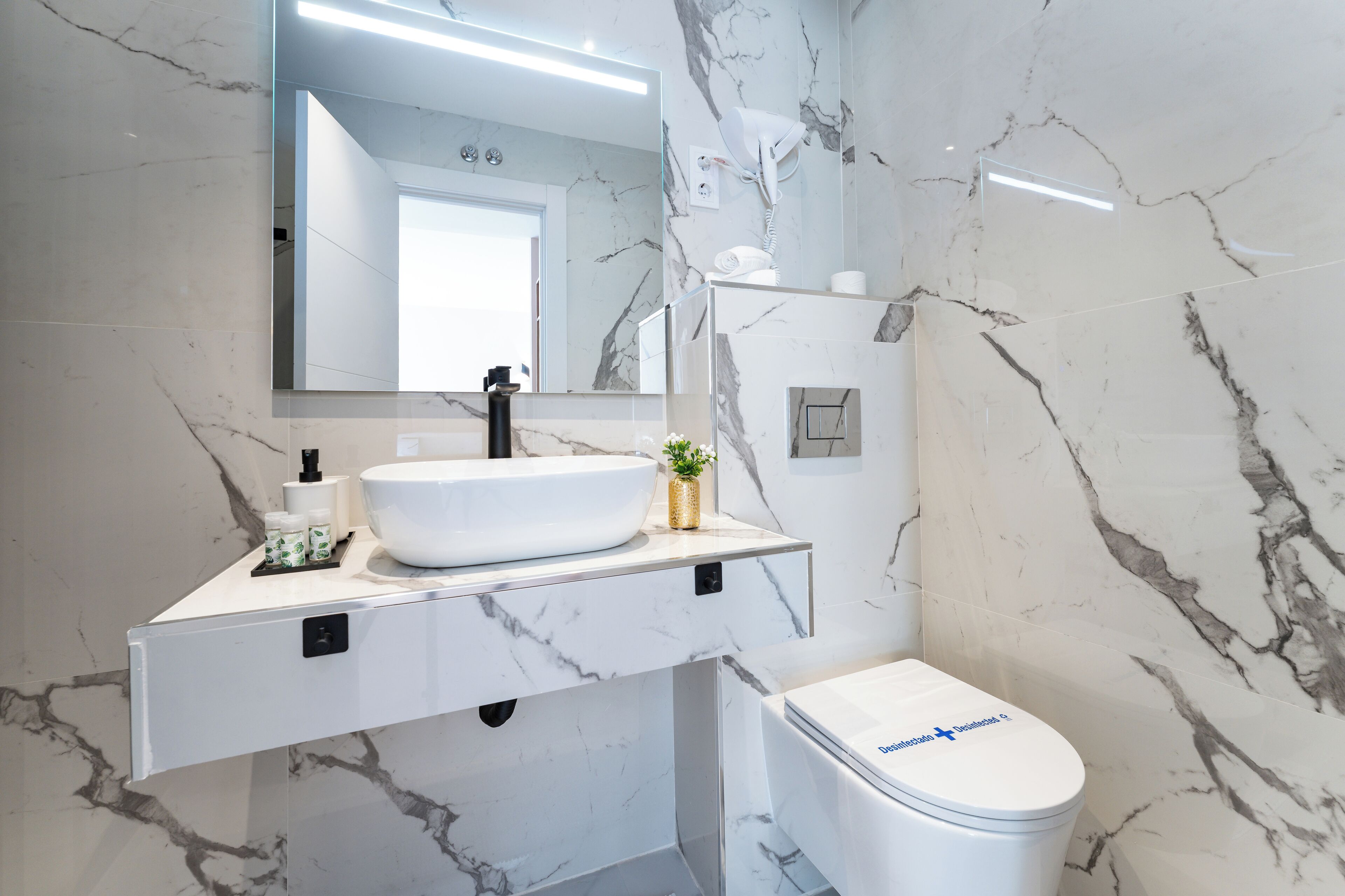 A modern bathroom with a white marble sink, a mirror, and a toilet.