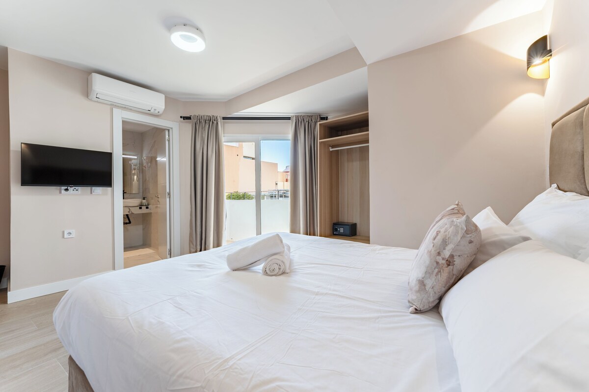 Een hotelkamer met een groot bed, een aan de muur bevestigde televisie, een airconditioning, een kledingkast en uitzicht buiten via een glazen deur.
