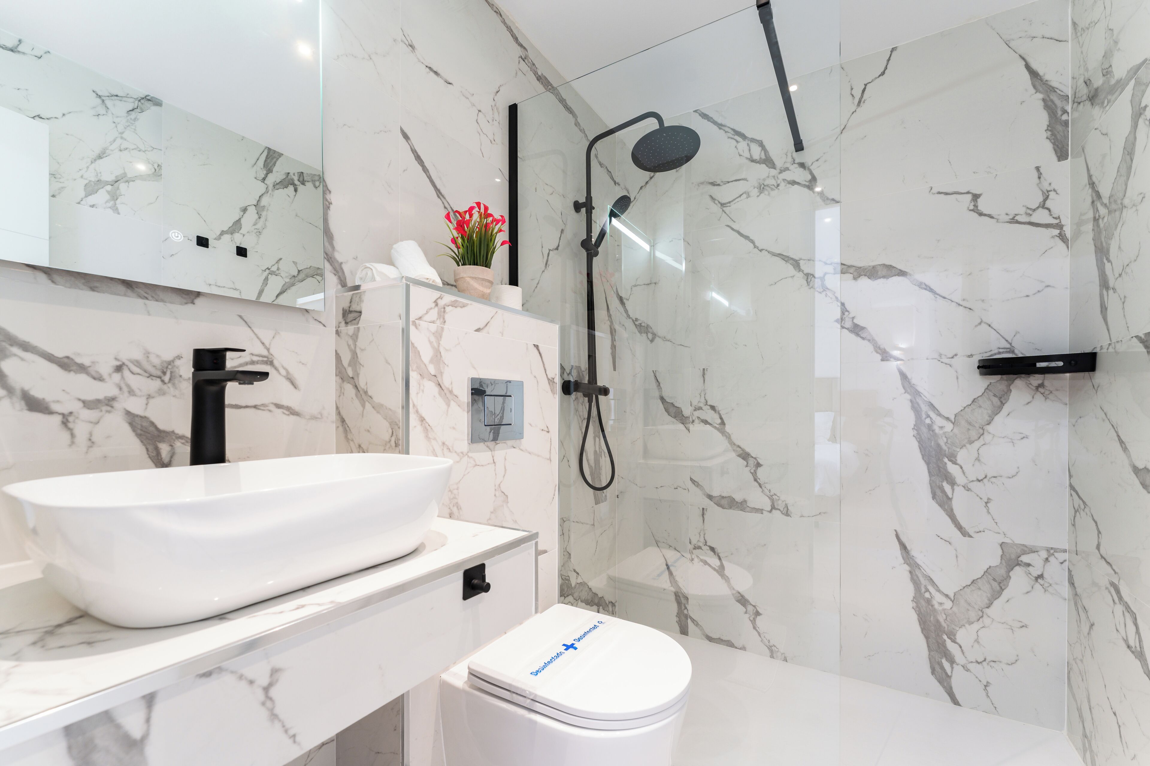 Un baño moderno con un lavabo de mármol blanco, un inodoro y una zona de ducha.