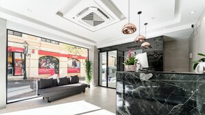 A modern lobby with a marble reception desk, a grey sofa, and large windows overlooking a street. - blanca maris (Fuengirola)