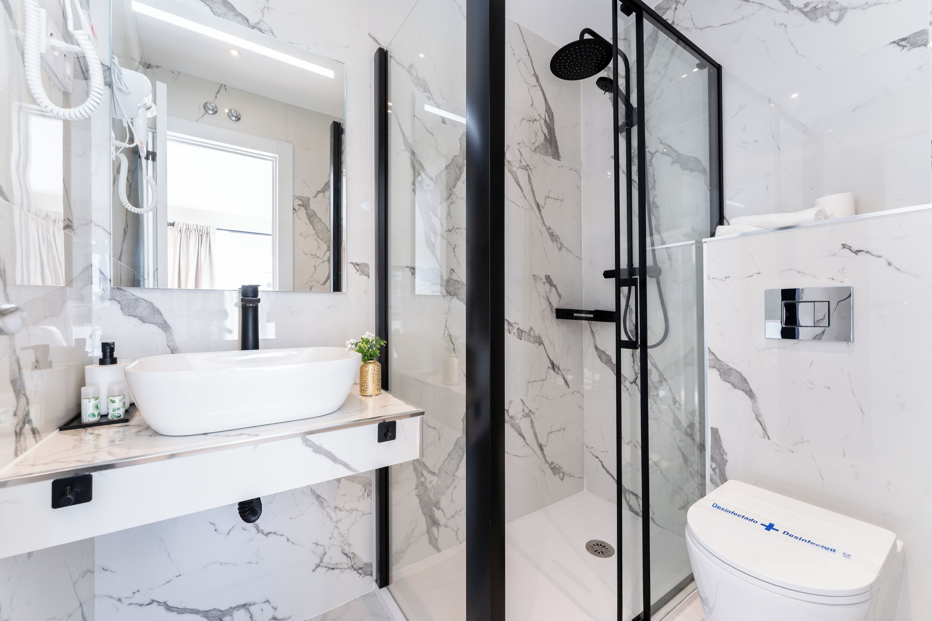 Un baño moderno con un lavabo grande y blanco, una cabina de ducha de vidrio y un inodoro con etiqueta de marca visible.