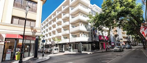 Un hotel de varios pisos con balcones, vista a la calle y cielo despejado.