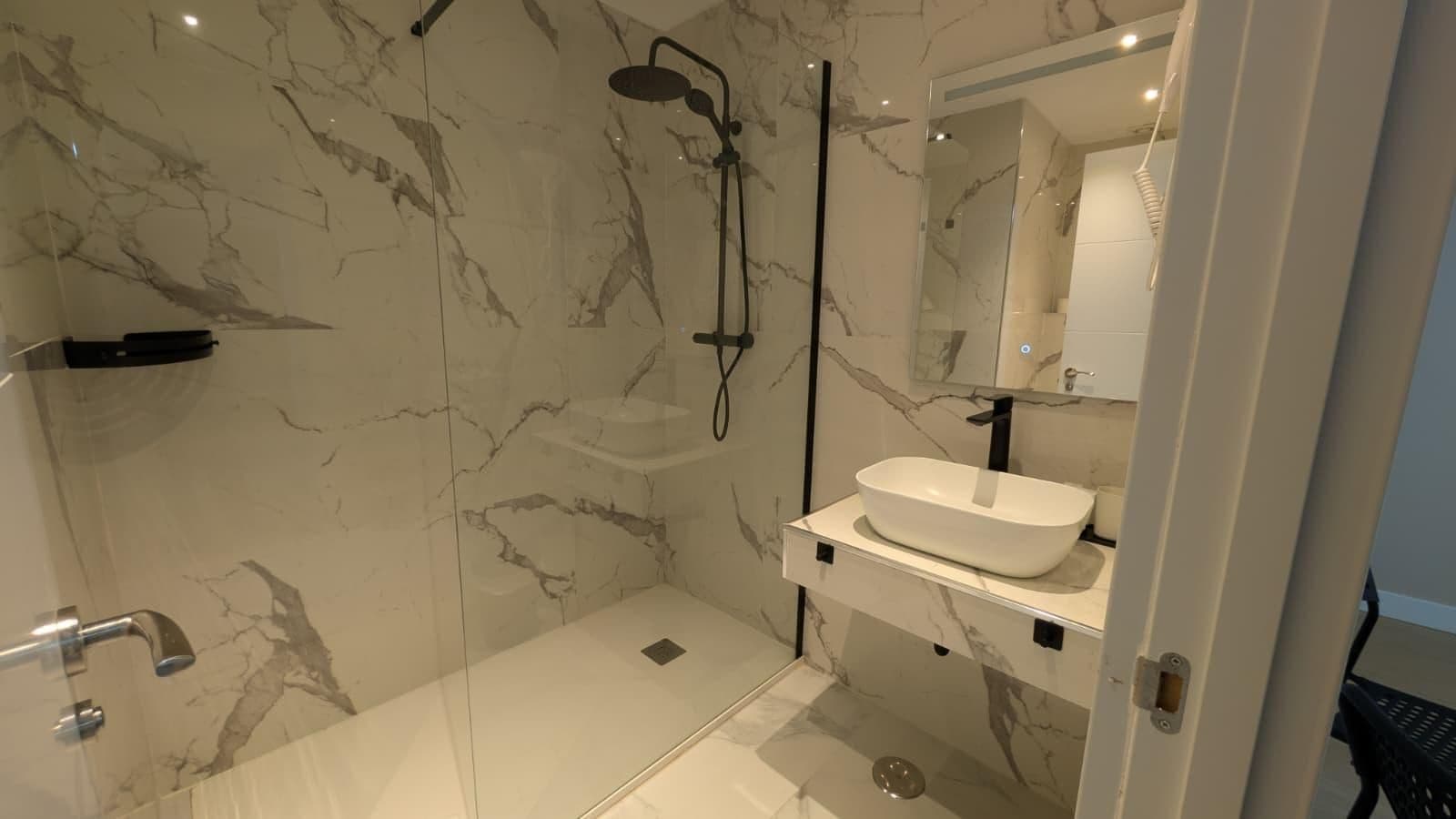 A modern bathroom with a glass shower enclosure, a white sink, and a marble backsplash.