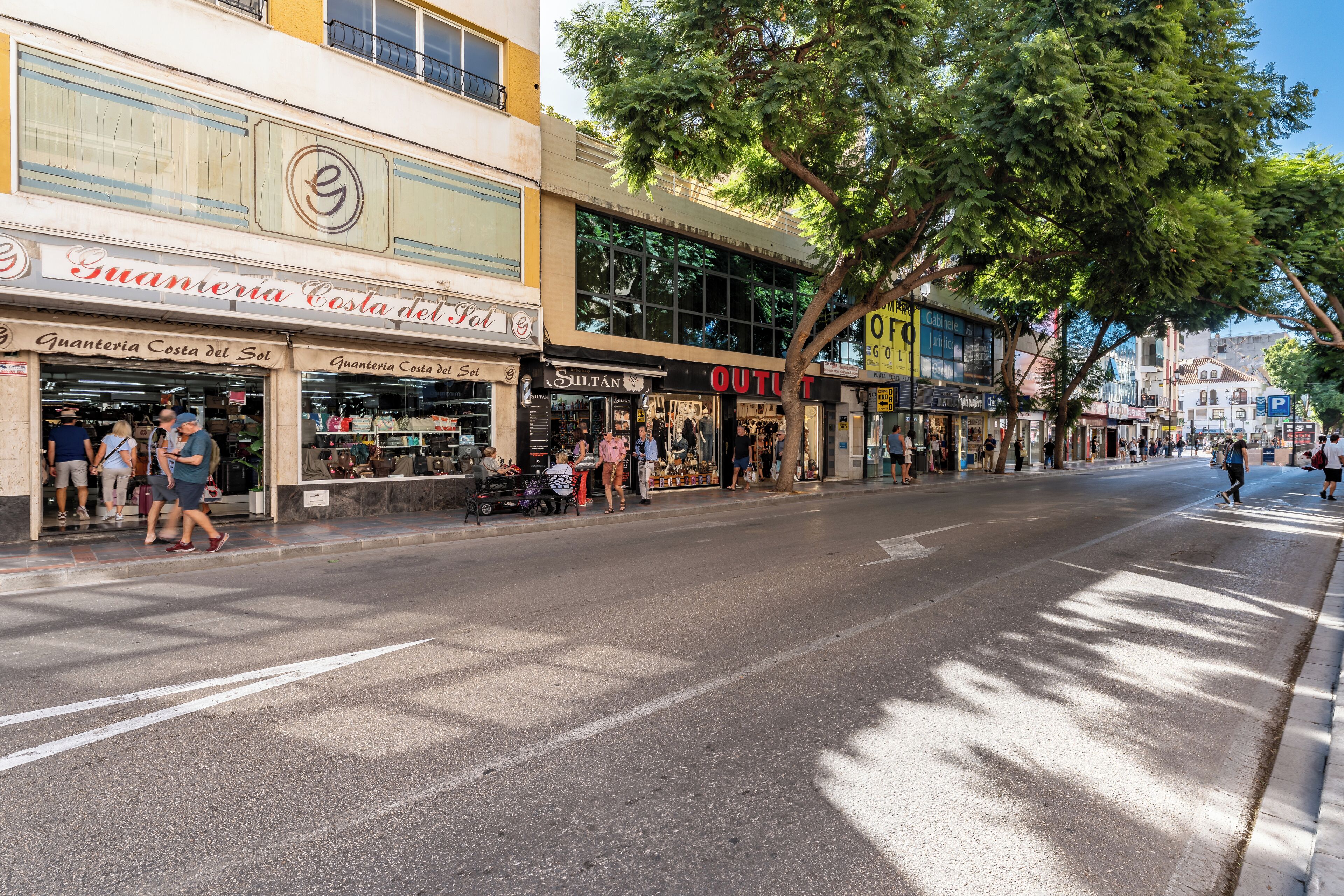 Una calle con locales comerciales, incluyendo 'Guanteria Costa del Sol' y 'Siltan Outlet'.