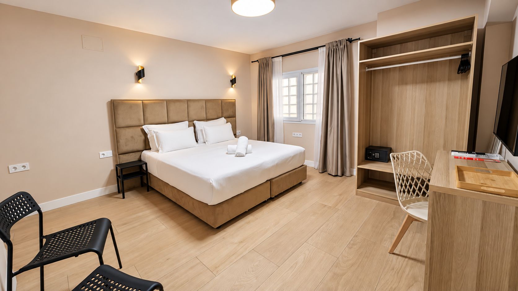 Quarto de hotel com cama, mesa de cabeceira, cadeira, guarda-roupa e escrivaninha com bandeja.