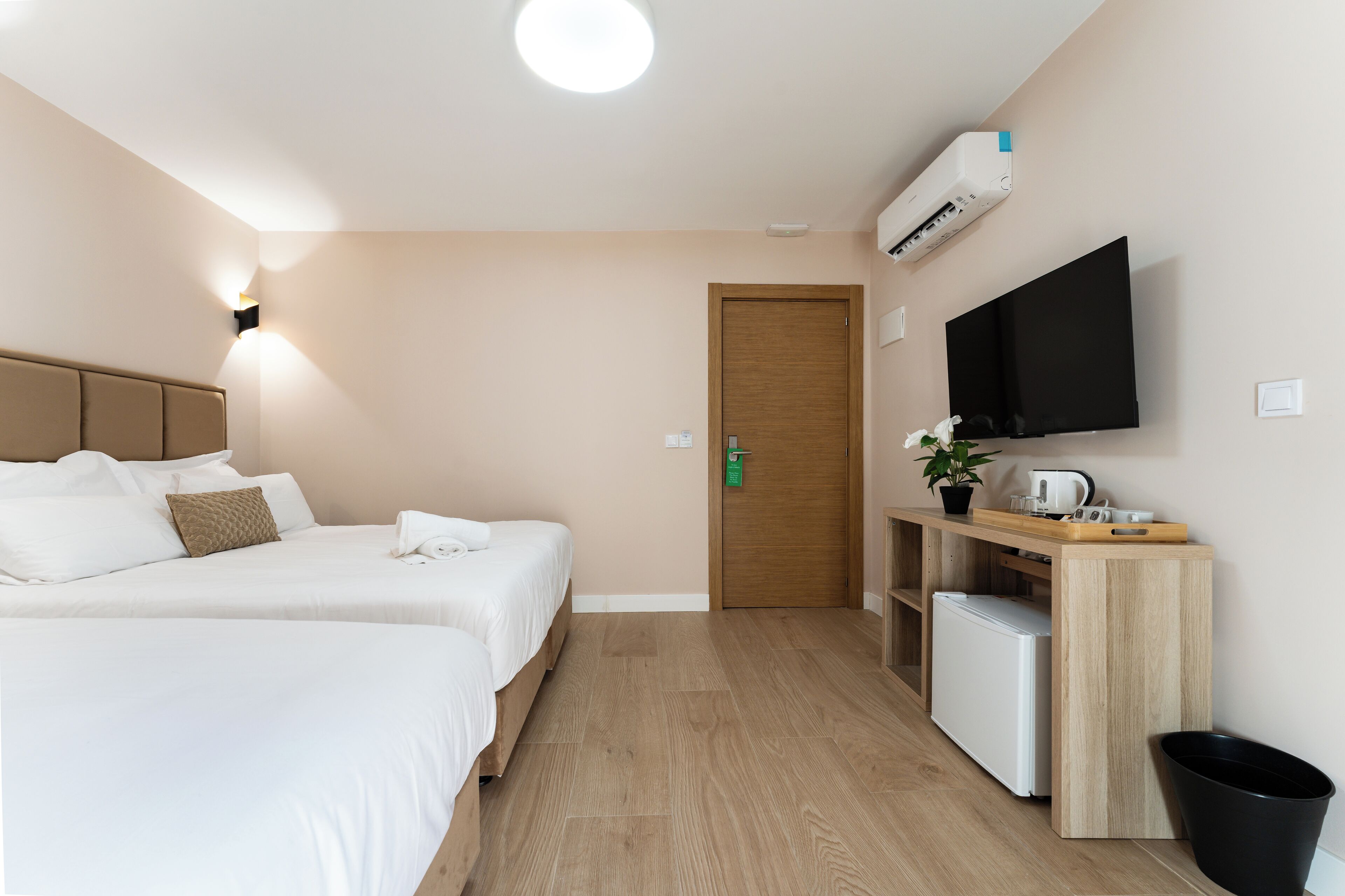 A hotel room with two beds, a TV, a small kitchenette, and a wooden door.