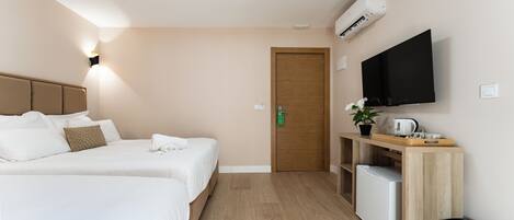 Habitación de hotel con dos camas, televisión, kitchenette pequeña y puerta de madera.