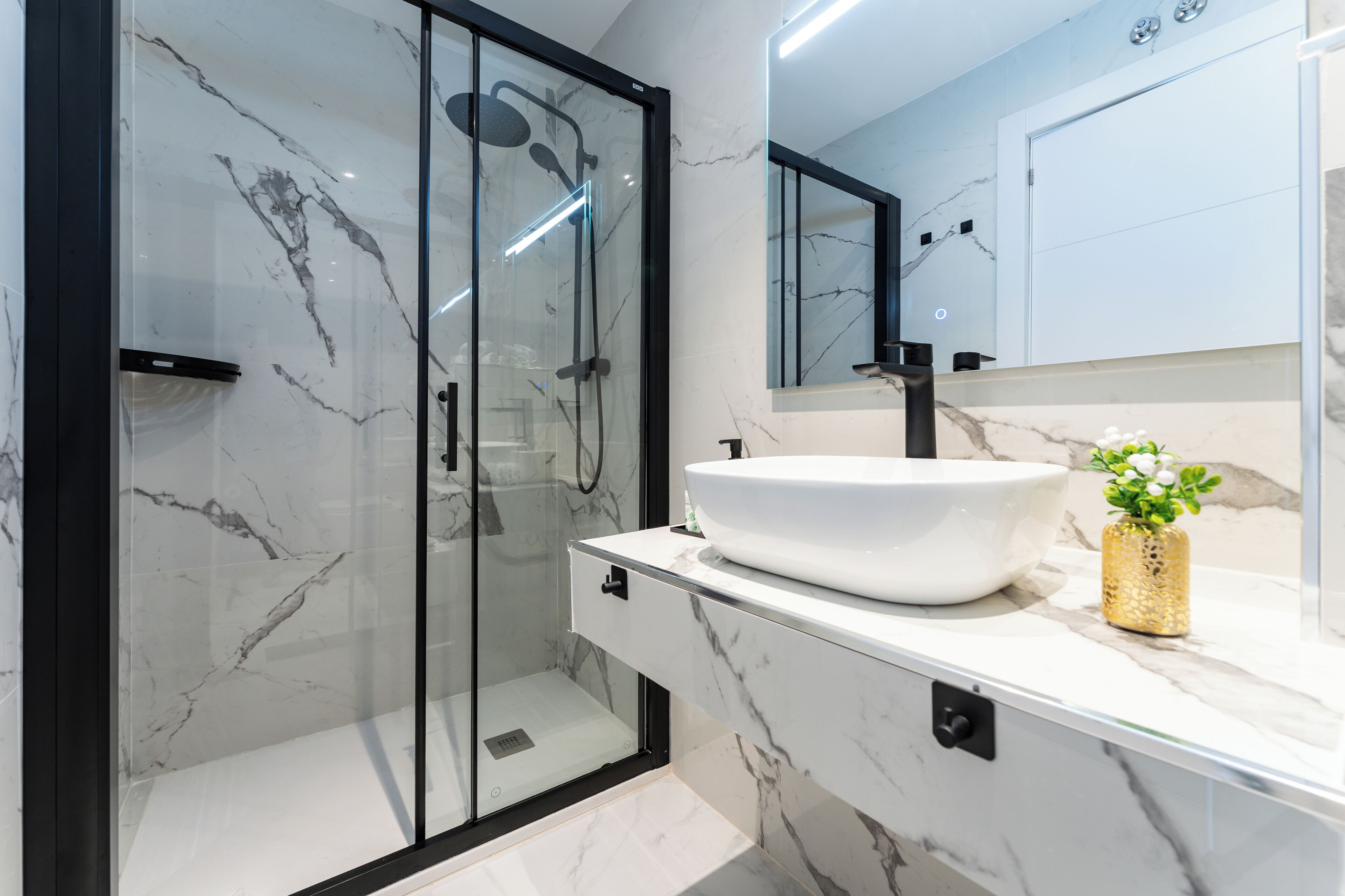 Un baño moderno con ducha de vidrio, lavamanos blanco y salpicadero de mármol.