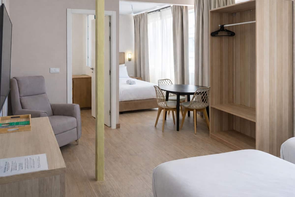 A hotel room with a bed, a desk, a chair, a table, and a wardrobe.