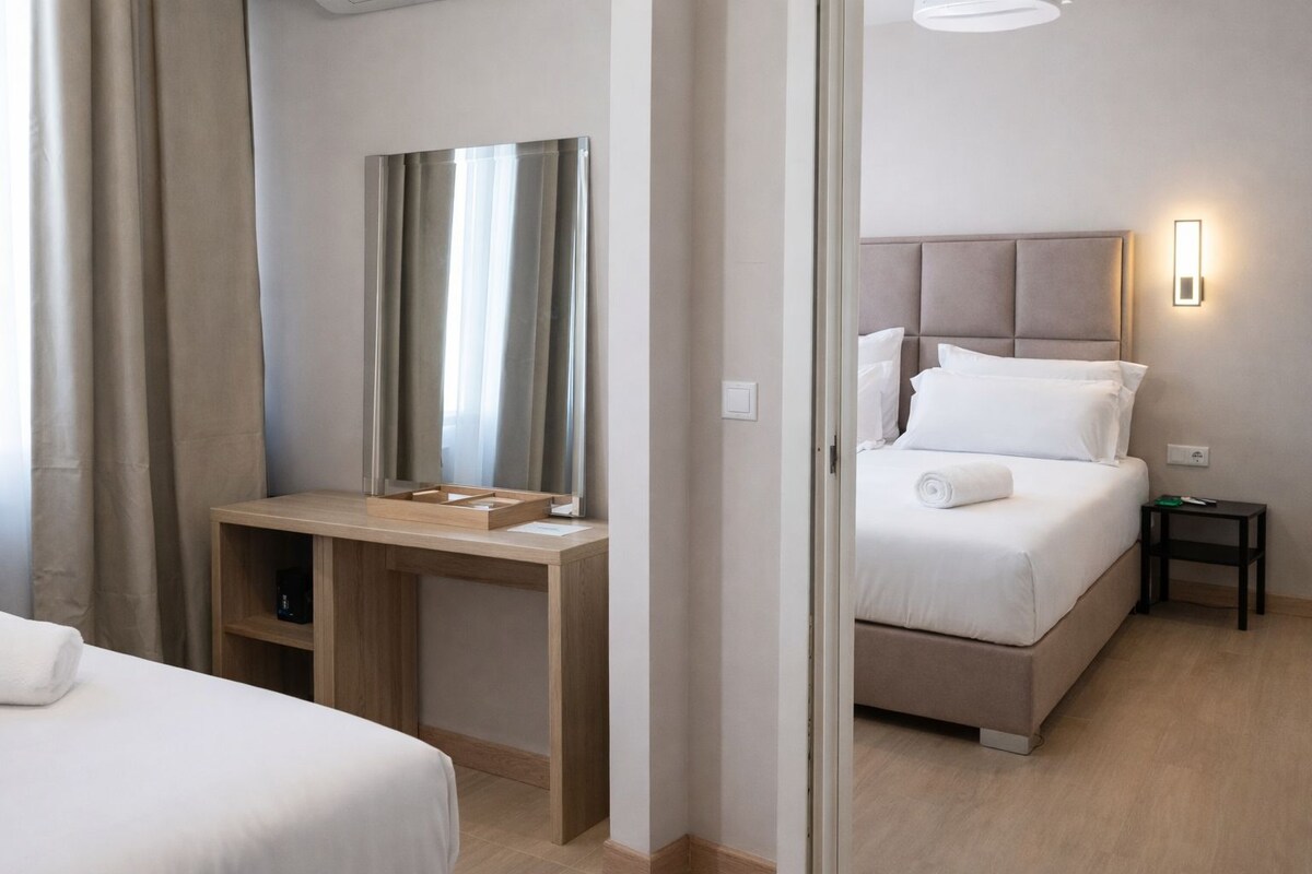 Een hotelkamer met een bed, nachtkastje, bureau met stoel, spiegel en een bijzettafeltje.