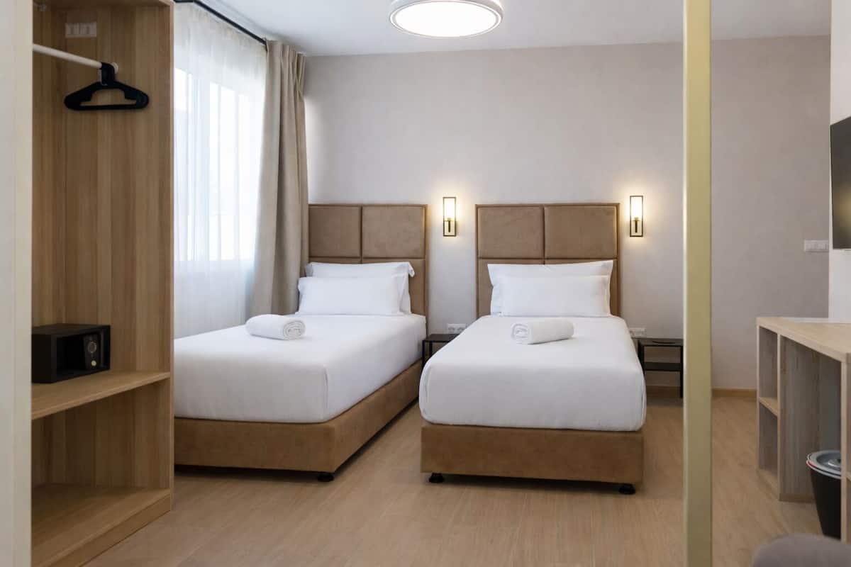 A hotel room with two beds, a wooden wardrobe, a desk, and a mirror.