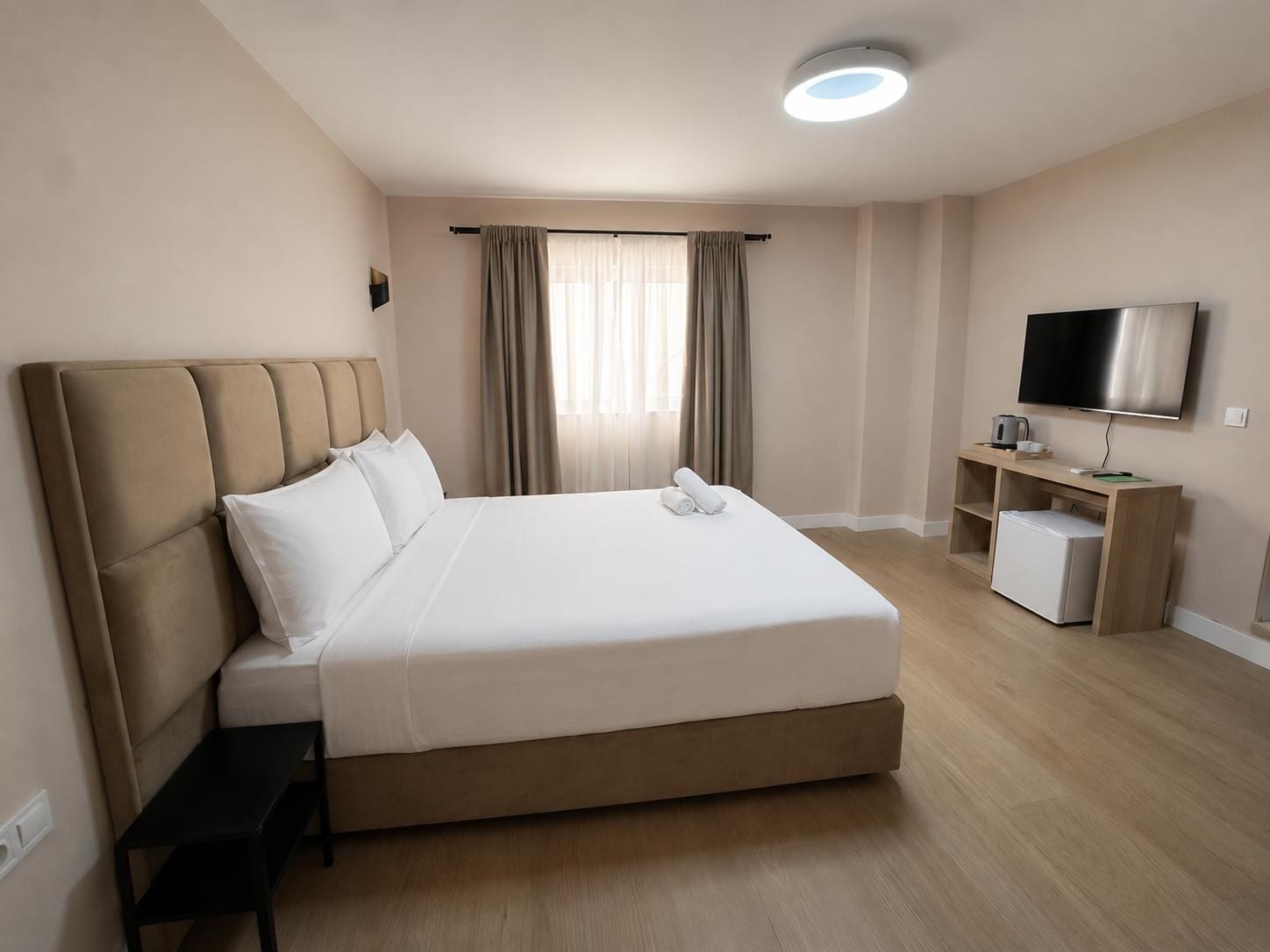 A hotel room with a large bed, a television, a desk, and a small refrigerator.