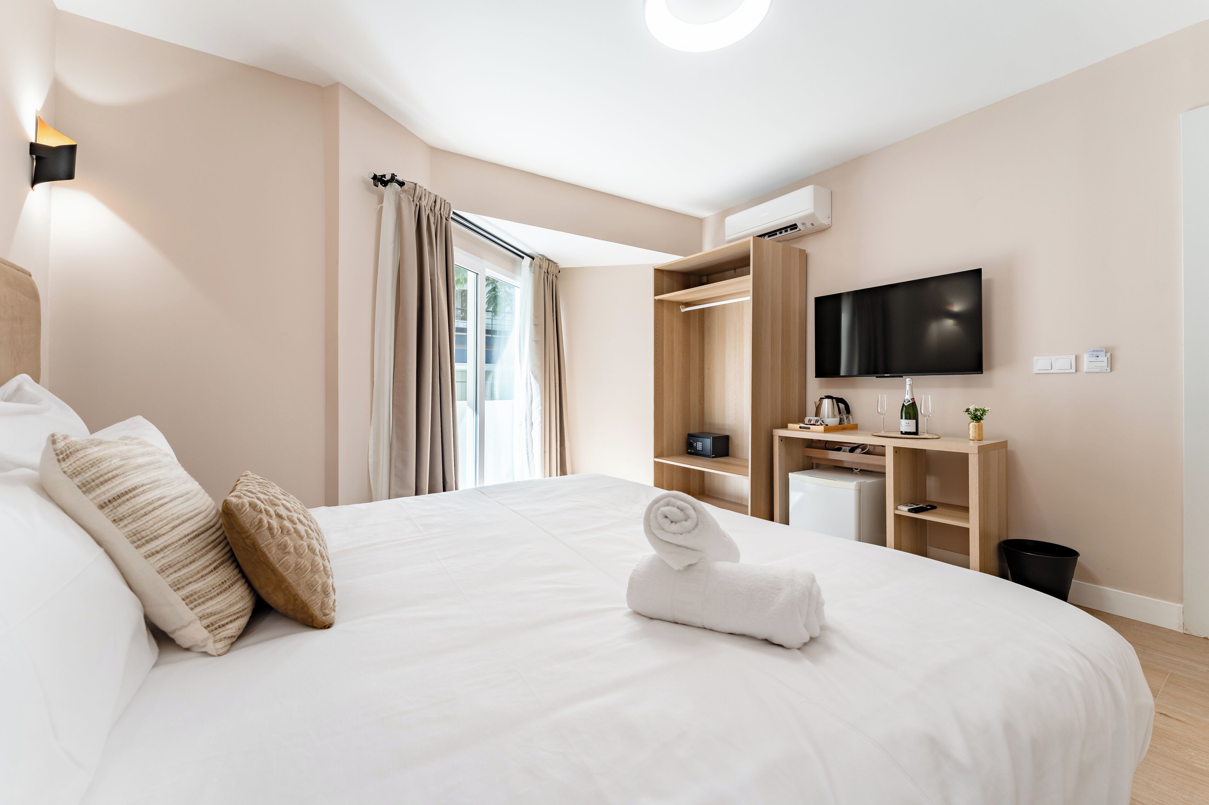 Ein modernes Hotelzimmer mit einem großen Bett, einem Fernseher, einem Schreibtisch mit Computer und einem Kleiderschrank.