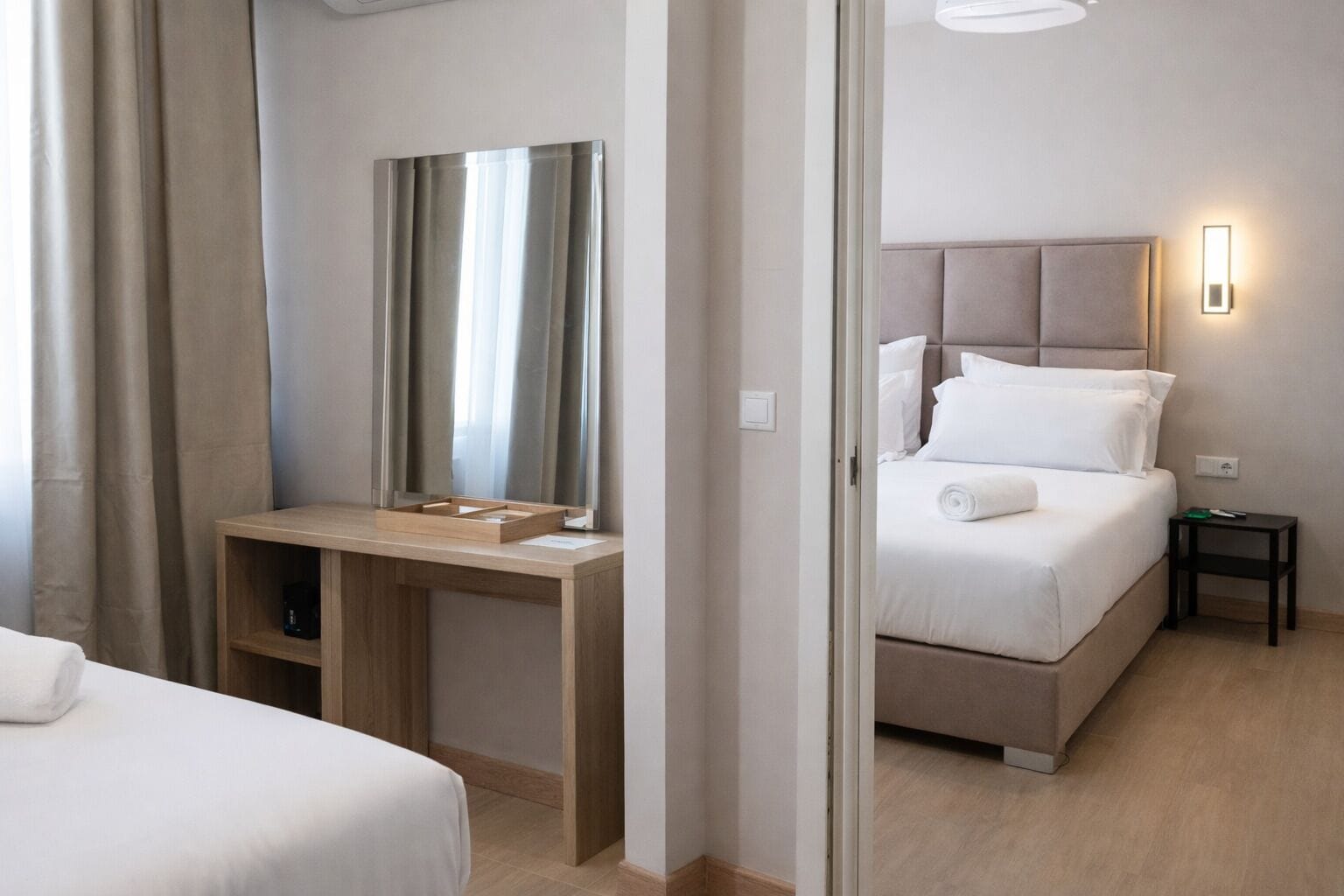 A hotel room with a bed, a bedside table, a desk with a chair, a mirror, and a nightstand.