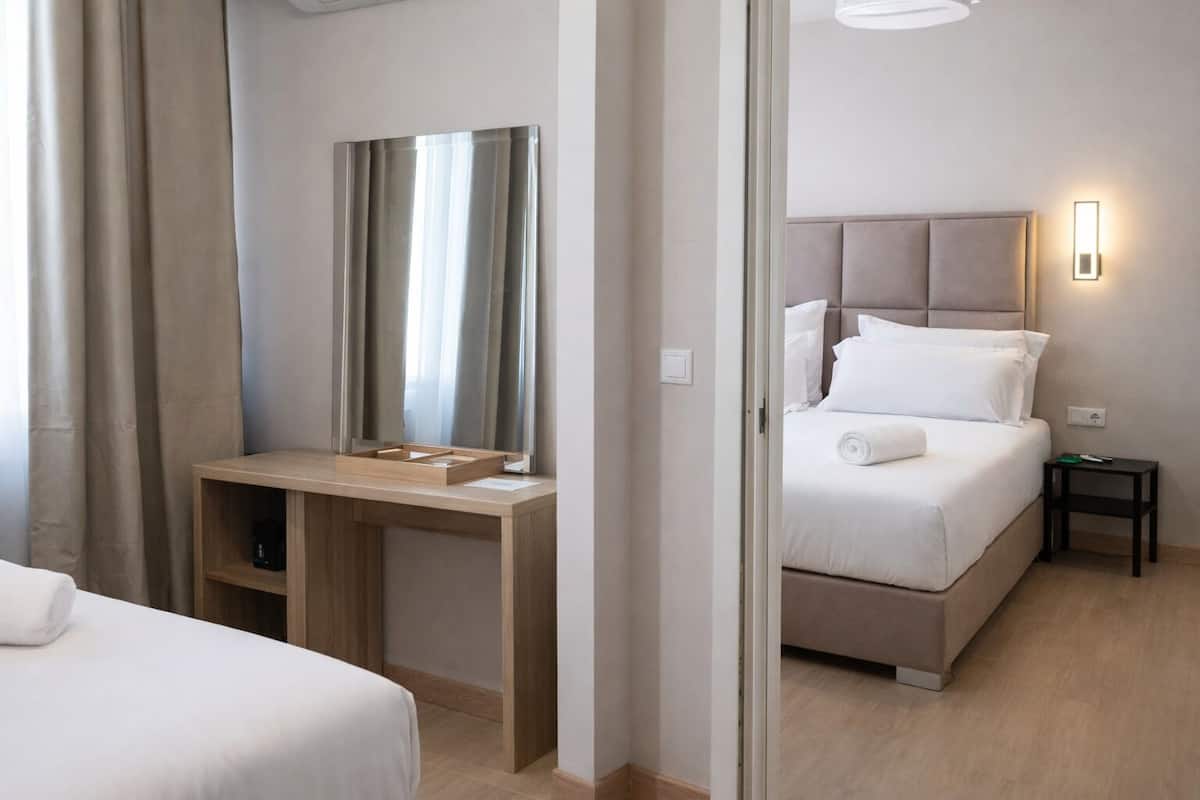 A hotel room with a bed, a bedside table, a desk with a chair, a mirror, and a nightstand.