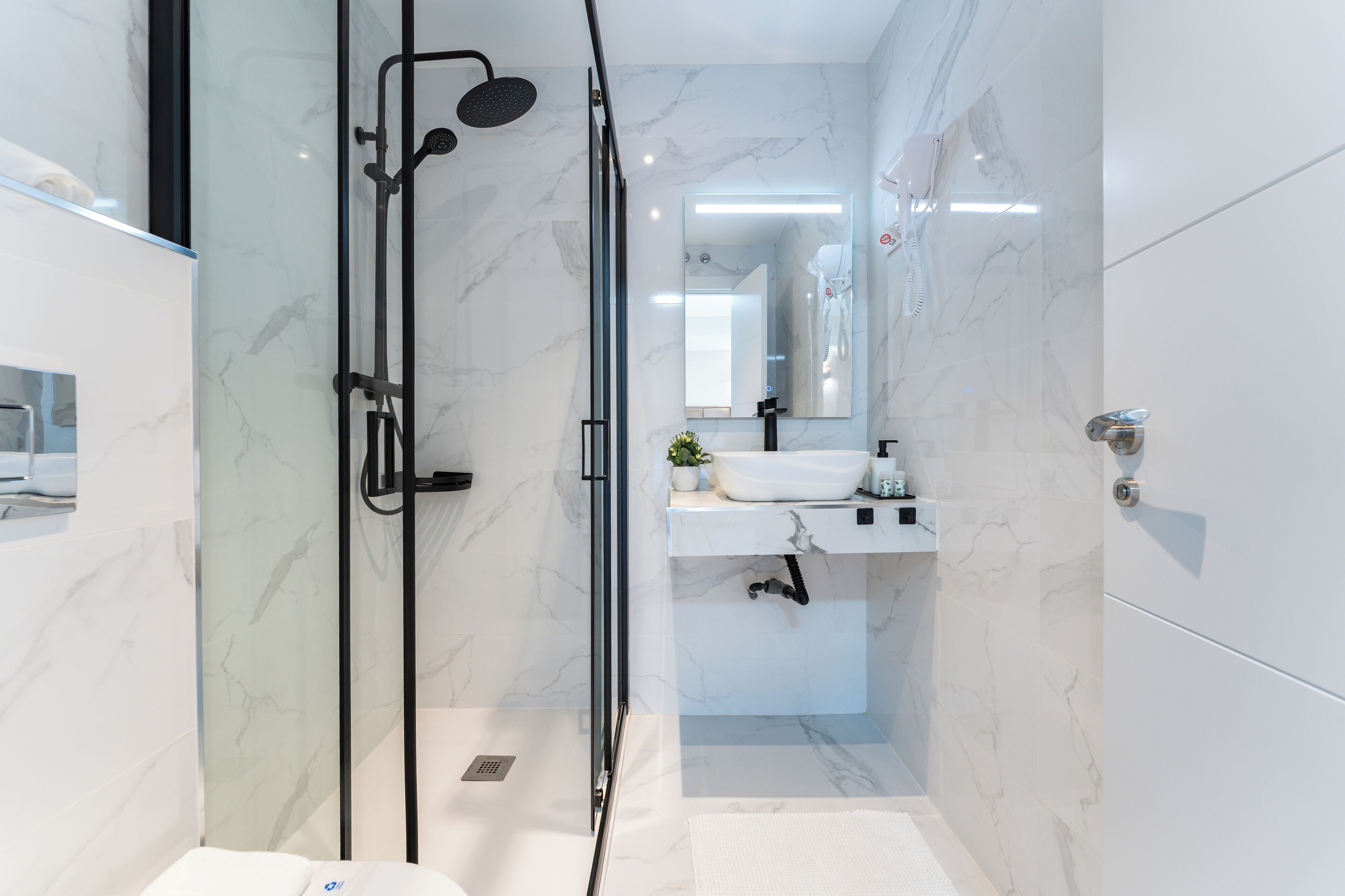 Une salle de bain moderne avec une douche en verre, un lavabo blanc et un miroir au-dessus du lavabo.