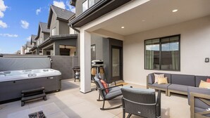A modern outdoor patio area with a hot tub, seating, and a stone feature. - Long Drive: Private Hot Tub + Resort Amenities (Washington)