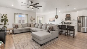 A modern living room with a sectional sofa, a dining area with bar stools, and a kitchen with stainless steel appliances. - Long Drive: Private Hot Tub + Resort Amenities (Washington)