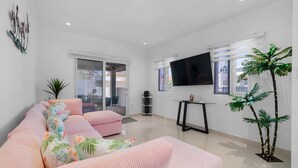Una sala de estar moderna con un sofá rosa, un televisor de pantalla plana y una alta palmera artificial.