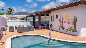 Piscina con un mural de cactus y flamencos, mobiliario exterior y un área de patio techada.