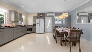 Una cocina moderna con armarios grises, un refrigerador blanco y una zona de comedor con una mesa y sillas de madera.