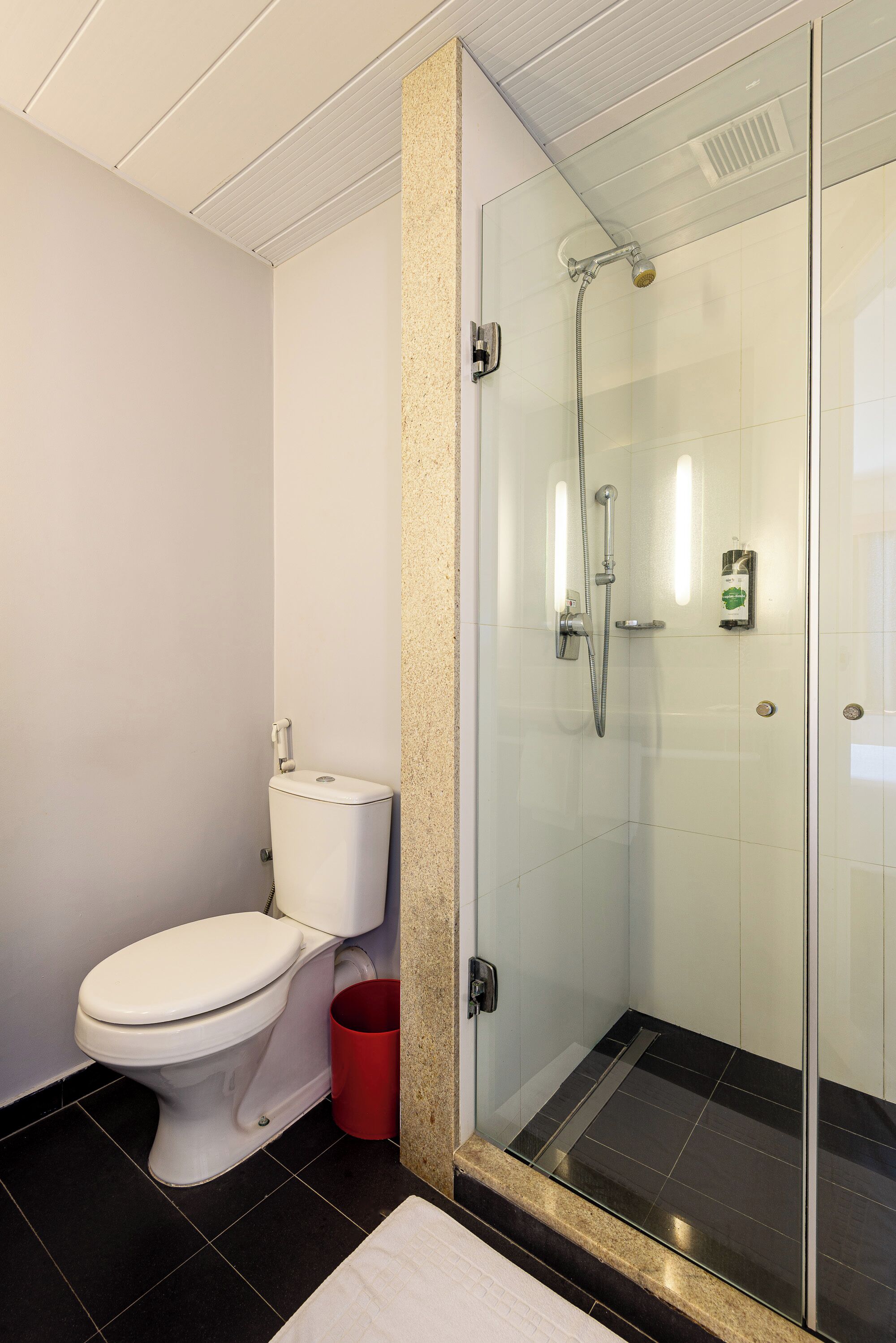A modern bathroom with a toilet, a glass shower enclosure, and a red trash bin.