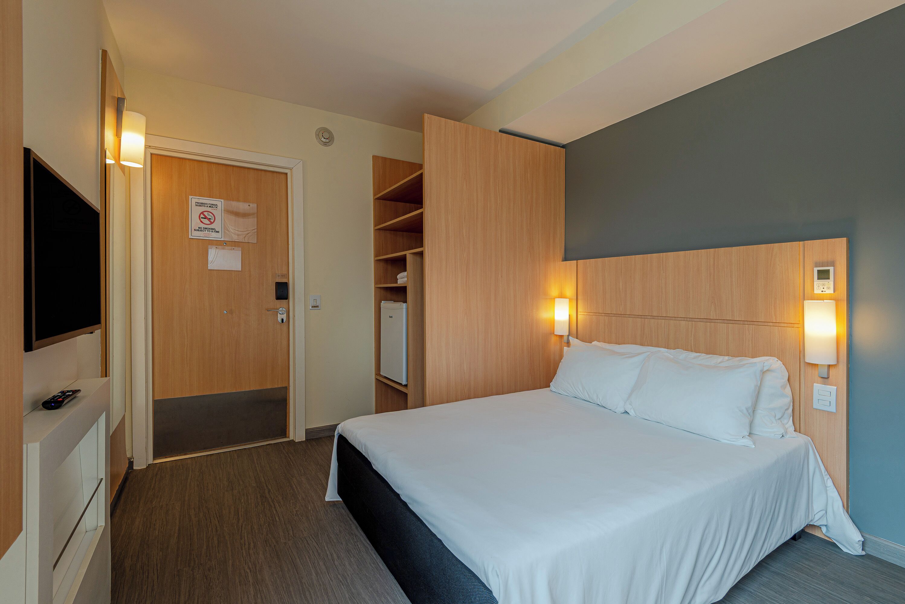 Habitación de hotel con cama, televisi ón, armario y un refrigerador pequeño.