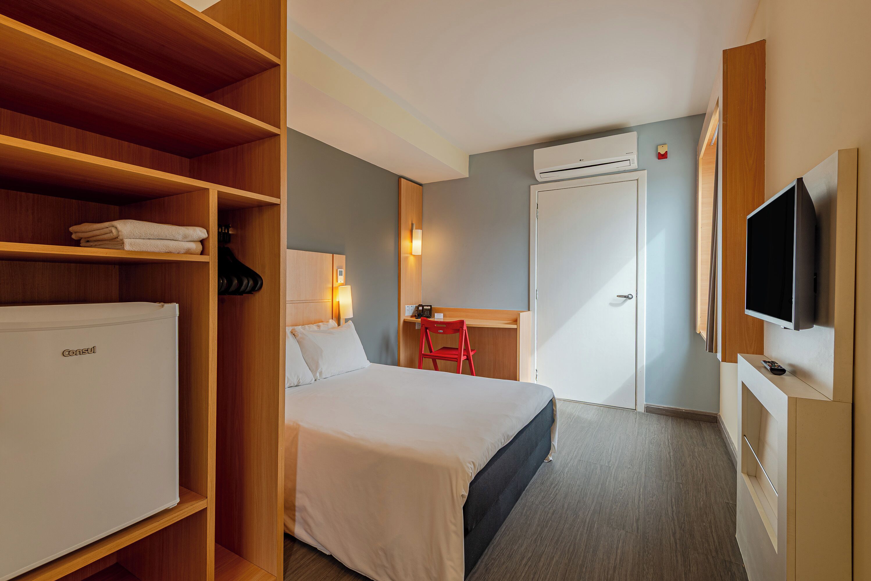A hotel room with a bed, a desk with a chair, a television, and a wardrobe.