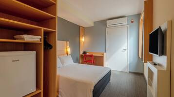 A hotel room with a bed, a desk with a chair, a television, and a wardrobe.
