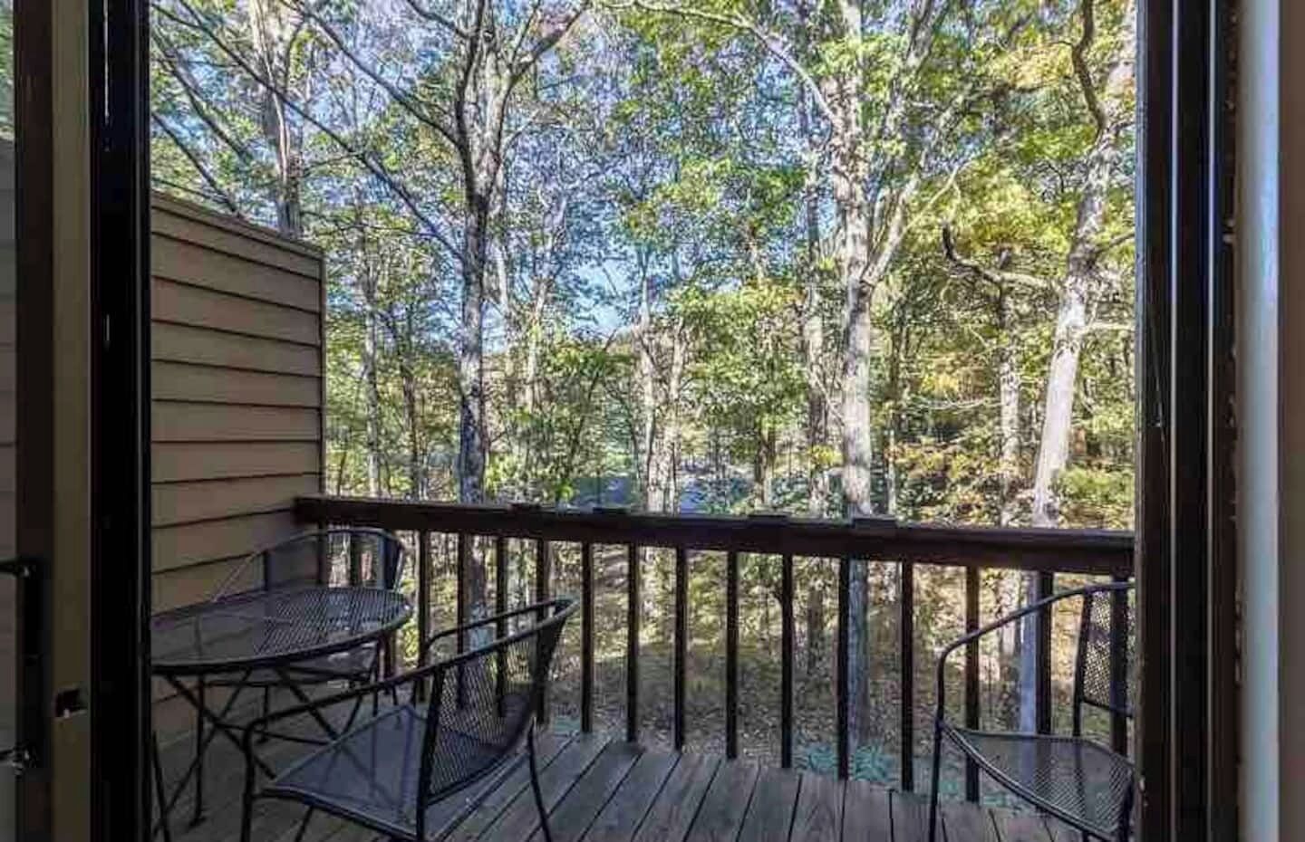 Eine Holzterrasse mit Metallstühlen und einem Tisch, mit Blick auf ein bewaldetes Gebiet.