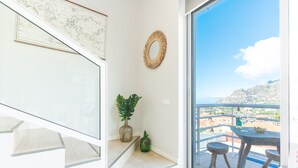 Un balcon avec une table, deux tabourets, une plante en pot et un miroir décoratif.