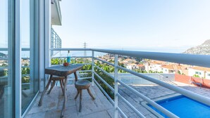 Un balcon avec une table et des chaises, donnant sur une piscine et une ville côtière.