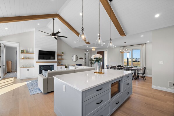 Una cocina amplia con una isla grande, vigas de madera, luces colgantes y un comedor con vistas.