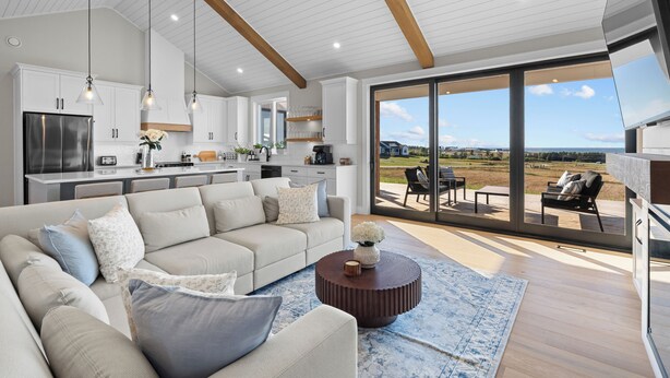 Un salon moderne doté d’un grand canapé, d’une table basse et offrant une vue sur l’extérieur grâce à de grandes portes-fenêtres coulissantes.