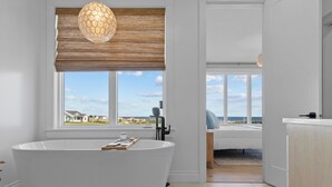 Une salle de bain moderne avec une baignoire sur pieds, un store en bois à la fenêtre et une vue sur la plage.