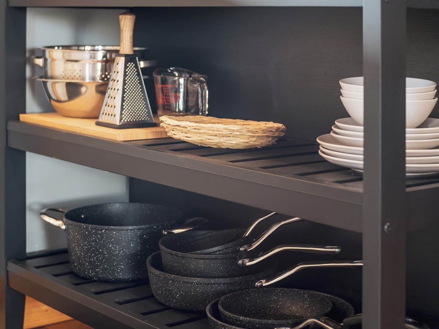 A kitchen shelf with cookware, a grater, and stacked bowls.