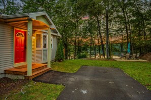 Une petite cabane avec une porte rouge, un porche et une allée pavée menant à un espace verdoyant où se trouvent une table et des chaises.