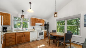 Una cocina con armarios de madera, una estufa blanca y una mesa de comedor con sillas.