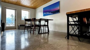 A spacious room with a wooden ceiling, a dining table with chairs, a bench, and a large window with a view of trees. - Unreal Mountain Views | Private Hot Tub | PÜR 3 (Golden)