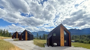 A modern cabin with a sloped roof, a wooden exterior, and a gravel driveway. - Unreal Mountain Views | Private Hot Tub | PÜR 3 (Golden)
