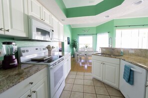 Une cuisine avec des armoires blanches, un four à micro-ondes, une cuisinière, un mixeur et un évier.