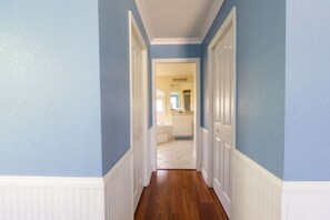 Un couloir aux murs bleus, aux boiseries blanches et au plancher en bois, qui mène à une cuisine.